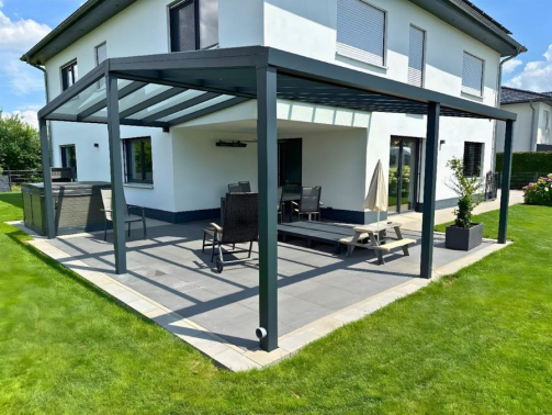 Glas-Terrassenüberdachung an einem modernen Haus, umgeben von einer Rasenfläche.