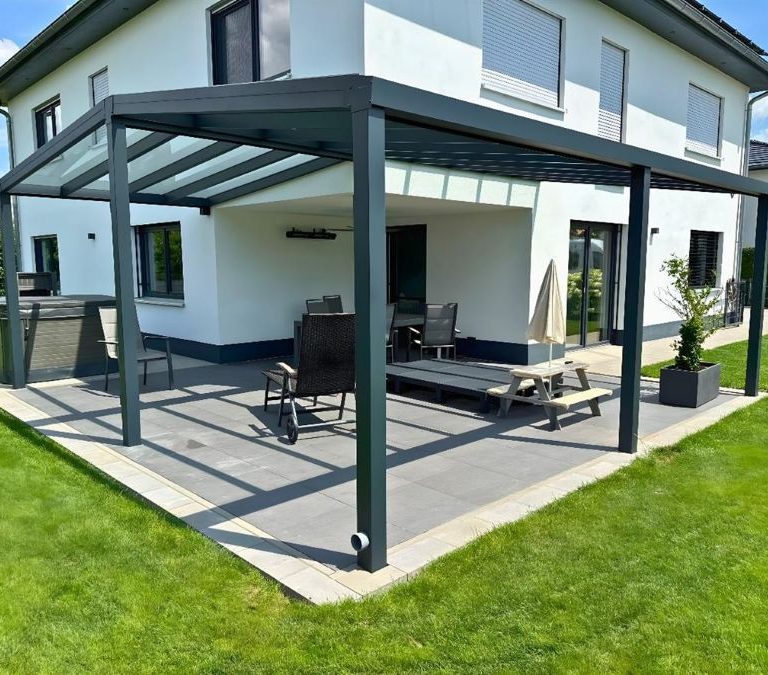 Glas-Terrassenüberdachung an einem modernen Haus, umgeben von einer Rasenfläche.