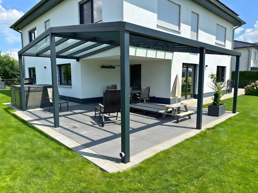 Glas-Terrassenüberdachung an einem modernen Haus, umgeben von einer Rasenfläche.